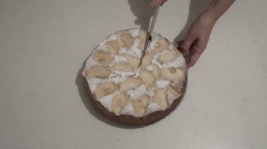 Kadın ev mutfağında beyaz bir masa üzerinde eşit parçalar halinde büyük bir bıçak ile yuvarlak bir Elmalı pasta kesmeye başlar. Üst te. Yakından kapatın. 4k