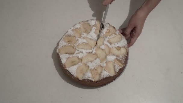 Η γυναίκα αρχίζει να κόβει μια στρογγυλή μηλόπιτα με ένα μεγάλο μαχαίρι σε ίσα κομμάτια σε ένα λευκό τραπέζι στην κουζίνα του σπιτιού. Κορυφαία προβολή. Κοντινό. 4K — Αρχείο Βίντεο