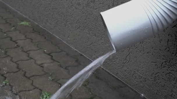 Extreme close-up van een witte afvoerpijp van waaruit een stroom van water giet op de bestratings platen tijdens de regen in de stad. Zijaanzicht. 4k — Stockvideo