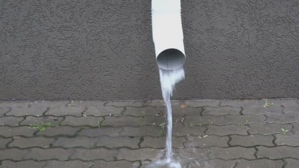 在城市的雨中，建筑物外墙上的排水管将一股水流倒在铺路板上。特写。4k — 图库视频影像