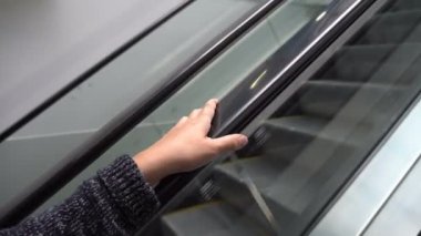 Yakın - şeffaf bir yürüyen merdiven sürmek ve korkuluk tutan bir kadının ellerini yukarı. Yukarı doğru hareket. Kavram. 4k.