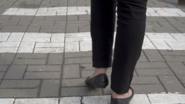 Yakın - siyah pantolon ve siyah ayakkabı kaldırım boyunca yaya geçidi boyunca yürüyen bir kadının bacaklarını kadar. Arka görüş. Zemin seviyesi görünümü. 4k.