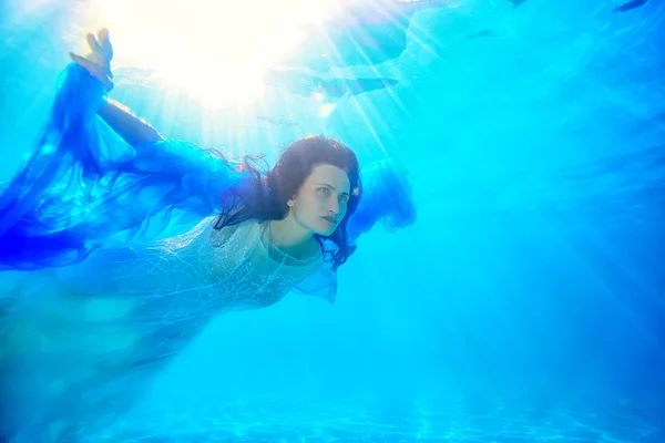 Ongewone bruid met haar haren zweven onder het water in het zwembad met een blauwe doek in haar handen in een witte trouwjurk. Ongebruikelijke bruiloft. Mode portret. Close-up. Surrealisme. — Stockfoto