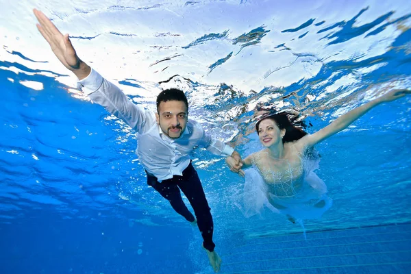 Joven chico feliz y chica en trajes de novia nadar y posar bajo el agua en la piscina con los brazos extendidos. Retrato. Concepto . — Foto de Stock