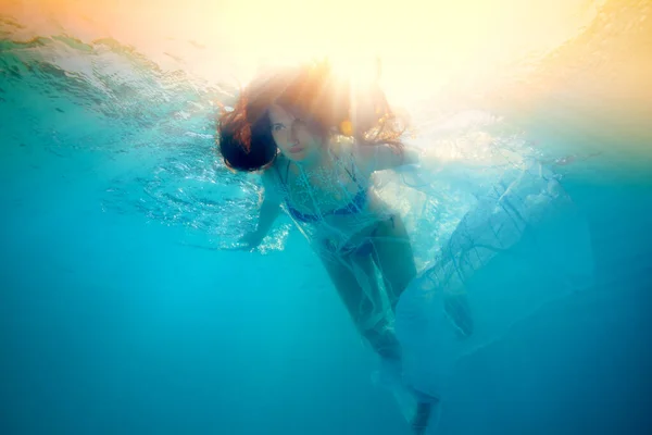 Une belle fille nage sous l'eau dans les rayons lumineux du soleil. Elle flotte avec ses cheveux vers le bas contre la lumière jaune vif de la surface. Portrait d'art numérique. Vue du bas — Photo