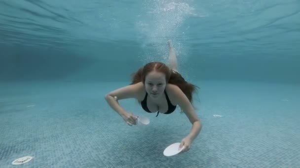 Une jeune fille douce nage sous l'eau avec de longs cheveux qui coulent et tenant une tasse blanche et une soucoupe. Elle regarde la caméra et les POP vers le haut. Au ralenti. Vue du bas. Prise de vue créative. 4K . — Video