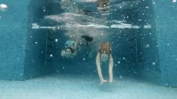 Tři roztomilé mladé dívky plavou pod vodou v bazénu a plavou spolu před kamerou. Sportovní trénink. Módní portrét. Zpomal. 4k. — Stock video
