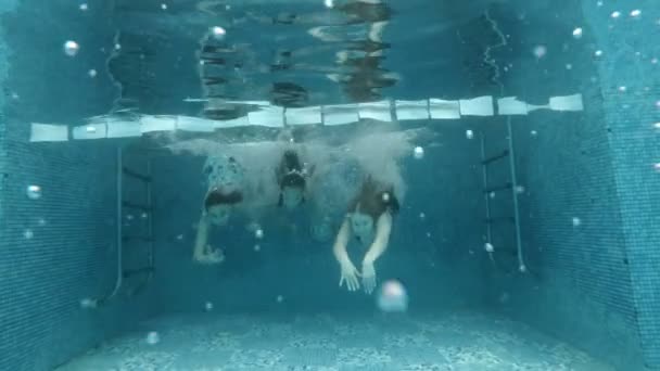 Due giovani ragazze e un bambino sono impegnati in sport acquatici. Si tuffano e nuotano sott'acqua nella piscina verso di me. Guardano la telecamera. Allenamento sportivo. Ritratto. Al rallentatore. 4K . — Video Stock
