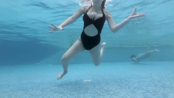 Een jong sexy meisje met lang stromend haar duikt onder water naar de bodem van een openbaar zwembad, kijkt naar de camera, zwaait met haar handen en drijft langzaam naar de oppervlakte. Portret. Een close-up. Langzame beweging. 4k. — Stockvideo