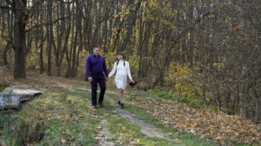 A pregnant couple, a young girl and a guy, walk through the autumn Park holding hands and kissing against the background of a beautiful landscape on a Sunny day. Family walk in nature. Concept. 4K