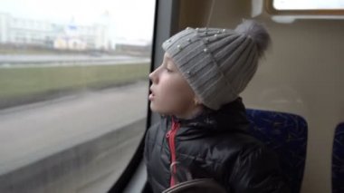 Küçük tatlı bir kız cama nefes alıyor ve bulutlu bir sonbahar gününde otobüsün sisli camına kalp çiziyor. Otobüs şehrin içinden geçer. Kavram. - Yakın çekim. 4K