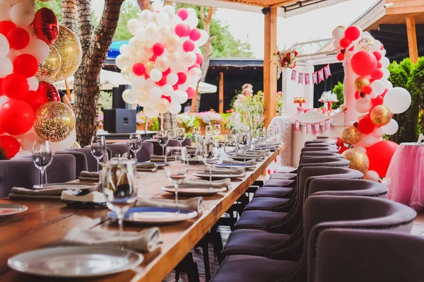 Served tables  for a birthday party in the restaurant in summertime, decorated with red and white balloons.