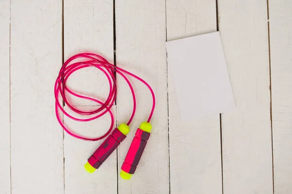 Sportswear on a white wooden background: notebook, jump rope. Healthy life concept. Top view.