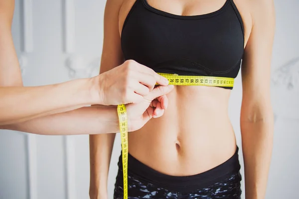 Personal trainer measuring a woman waist  at the fitness gym. Sport and dieting concept.