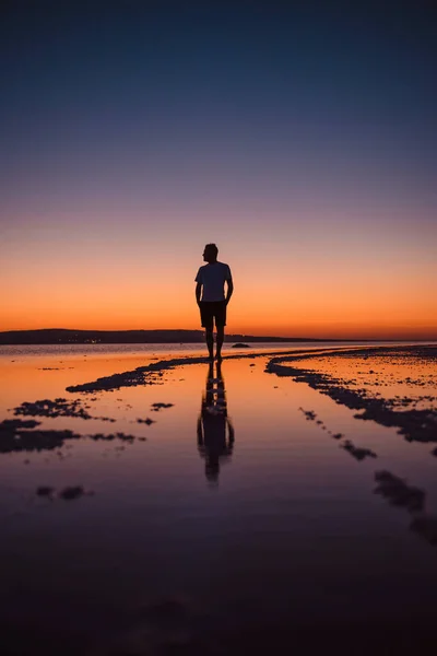 Silhouette of male traveller in summer outfit standing at salt lake in Turkey with amazing sunset behind. Reflection on water. Concept of adventure and travelling.
