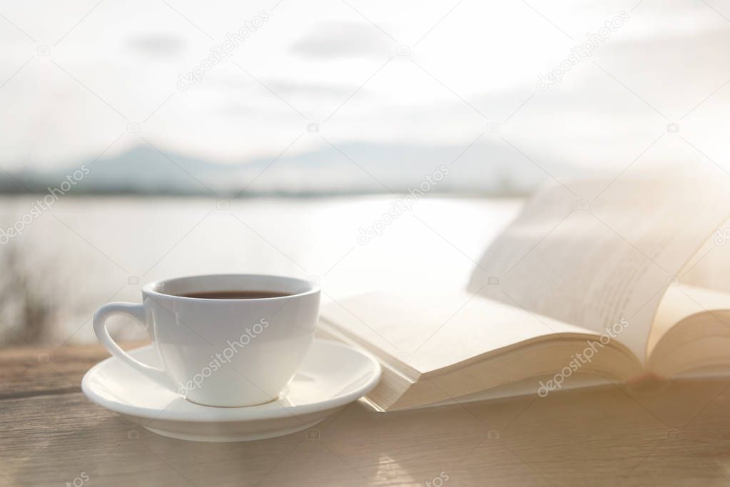 Cup of coffee and book on a wooden table in morning sunlight with a natural background