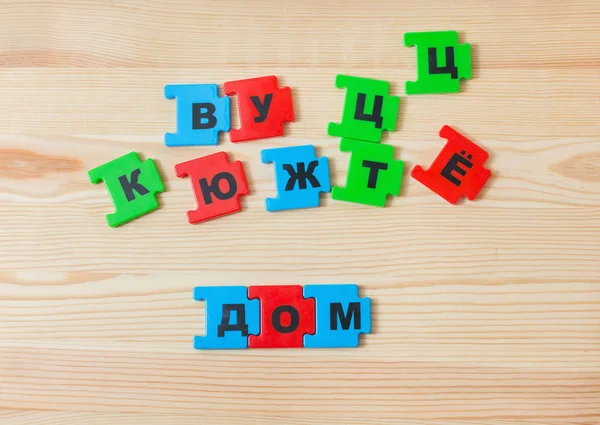 On a wooden background lie the letters of the Russian alphabet. The child laid out the inscription of the house in Russian