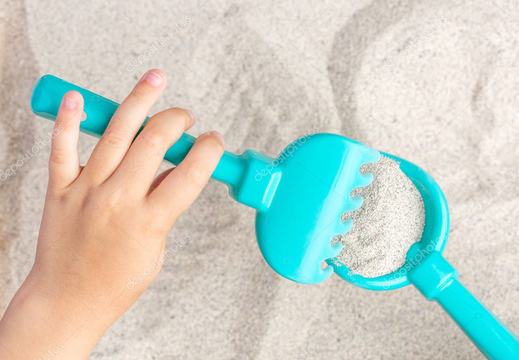 The child plays, manipulates with a shovel and rake with sea sand