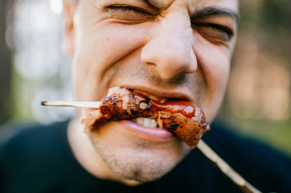 man eating grilled sausage in forest