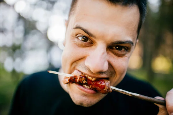 man eating grilled sausage in forest