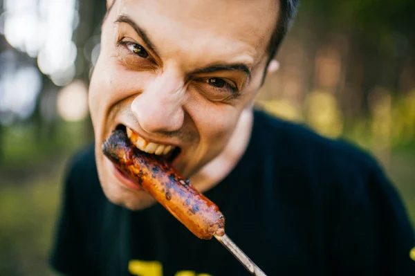 man eating grilled sausage in forest
