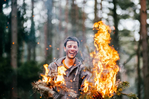 young man holding burning firewood in hands