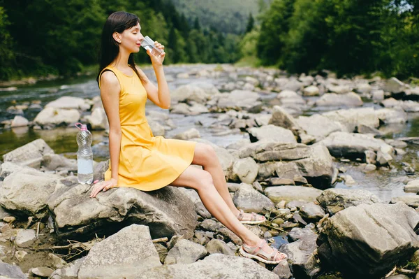 年轻的妇女在河岸喝水与石头在岸上 — 图库照片