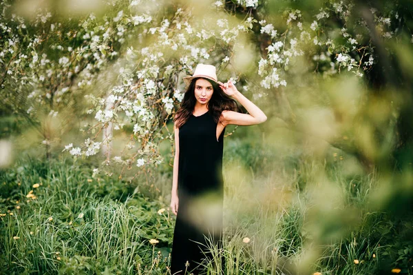春咲く庭でポーズの帽子と若いブルネットの女性 — ストック写真