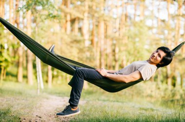 Genç adam hamakta güneşli gün yaz ormandaki rahatlatıcı