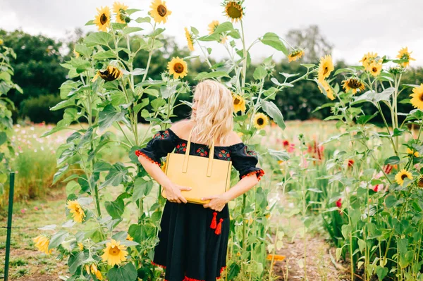 ひまわり畑でポーズをとって黄色の袋を持つ若い女性 — ストック写真