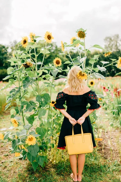 back view of woman with yellow bag posing in sunflower field