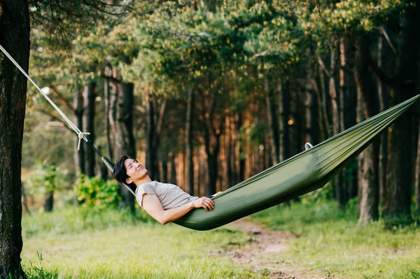 夏天阳光明媚的日子里 年轻人在森林的吊床里放松 — 图库照片