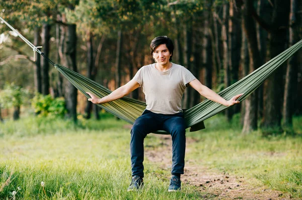 young man relaxing in hammock in forest on summer sunny day