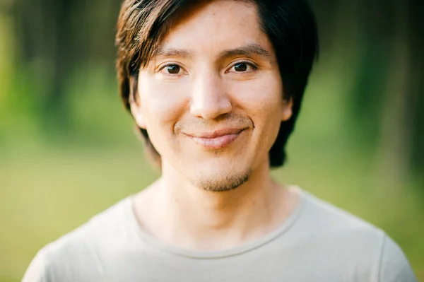 portrait of native american man with black hair and dark eyes looking at camera in forest
