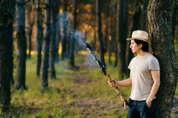 indian peruvian man in straw hat with smoking wooden torch in forest