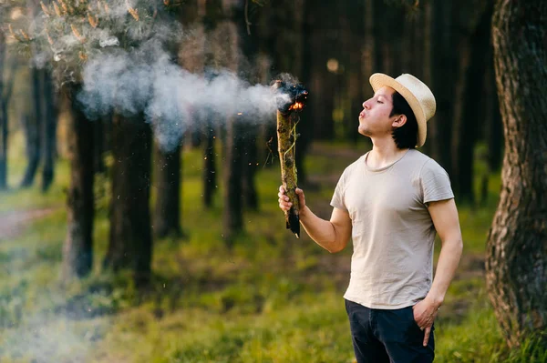 indian peruvian man in straw hat with smoking wooden torch in forest