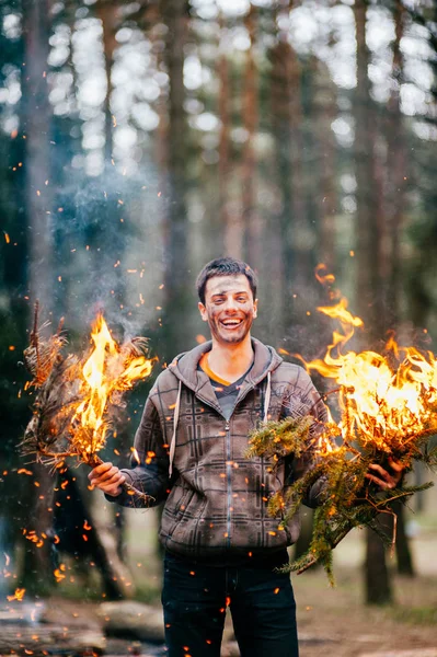 man holding burning firewood in forest
