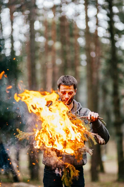 man holding burning firewood in forest