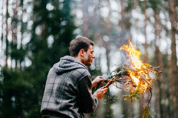 man holding burning firewood in forest