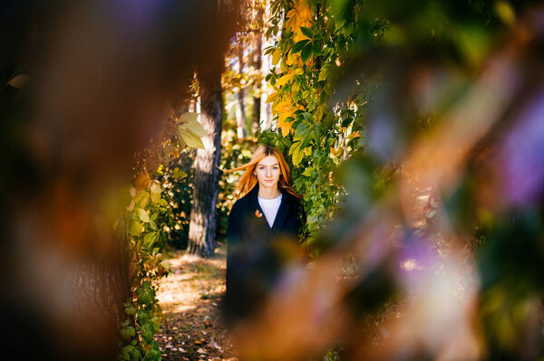 Young beautiful woman with red hair in autumn botanical garden with leaves around