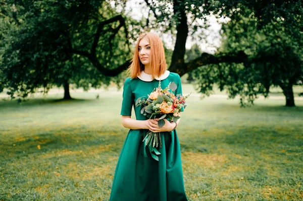 年轻的红头发女人在绿色礼服与夏天的花花束 — 图库照片