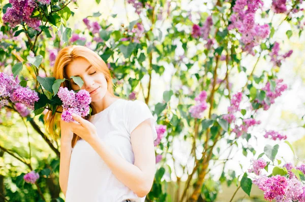 ライラック咲く公園の茂みで若い魅力的な女性 — ストック写真