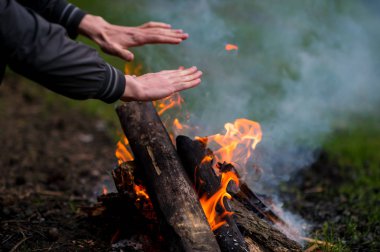 kısmi eller yakınındaki ormanda kamp ateşi yakma ısınma adam görünümünü 