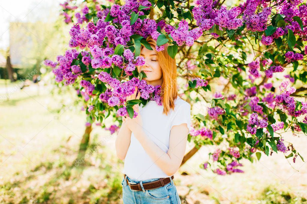 young attractive woman in park with blooming lilac bushes