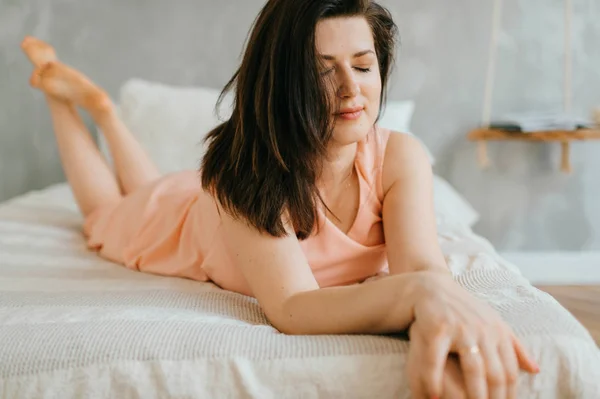 自宅で白いベッドに横たわっている美しいブルネットの女性 — ストック写真