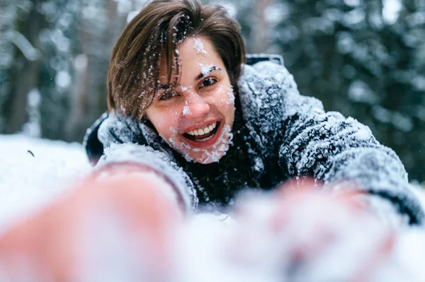 雪に覆われた冬の森の地面に横たわっている陽気な若い女性 — ストック写真