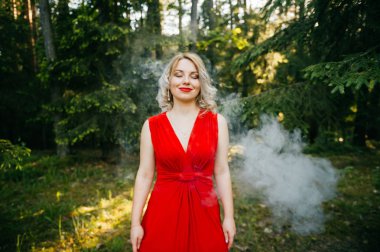 Kırmızı elbise ayakta bulutların duman ormandaki sarışın güzel genç kadın