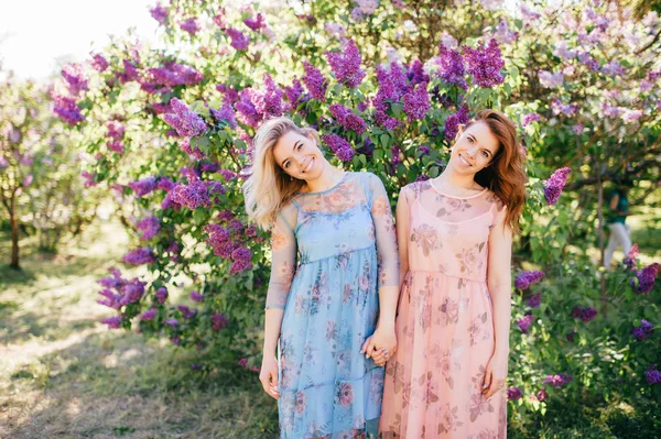開花の別のドレスで美しい若い双子の姉妹夏の植物園 — ストック写真