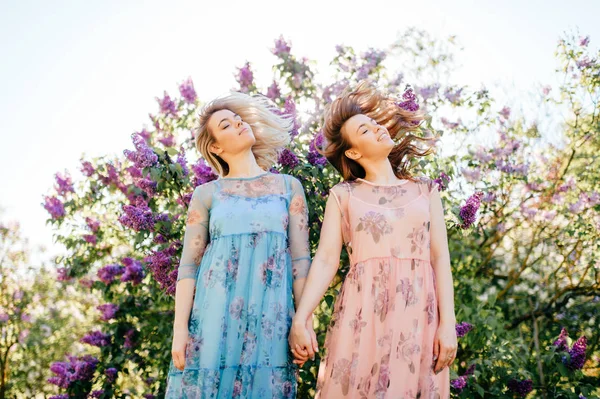 開花の別のドレスで美しい若い双子の姉妹夏の植物園 — ストック写真