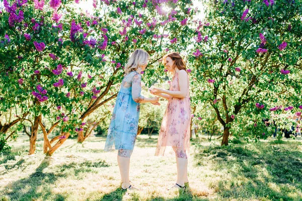 咲くの楽しみを持つ別のドレスの若い双子の姉妹夏の植物園 — ストック写真
